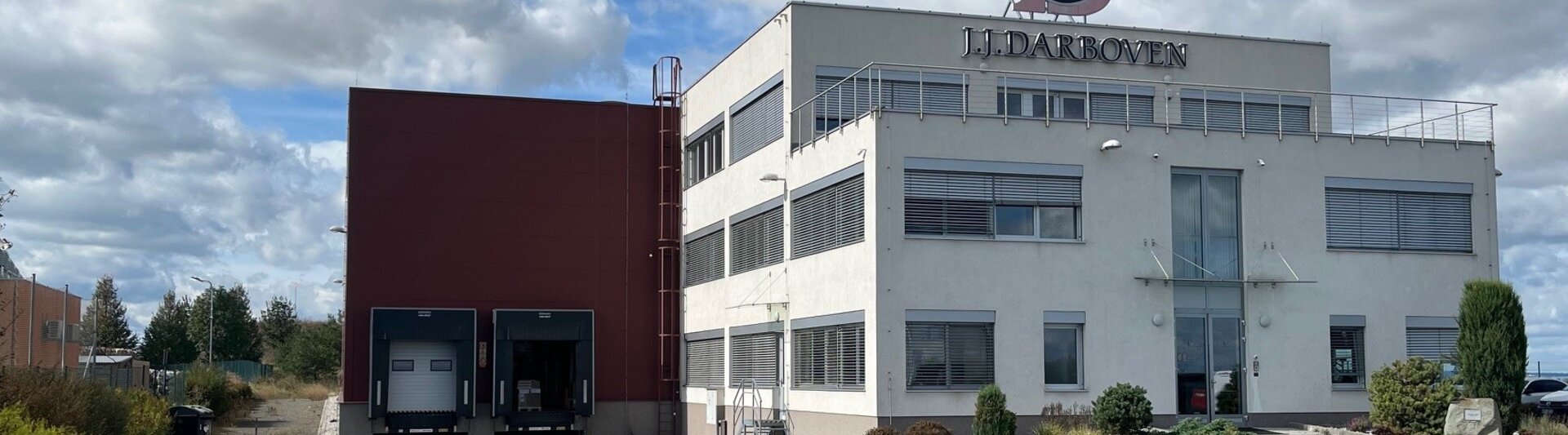 Moderní budova J.J. Darboven s nakládací plochou a upraveným okolím pod zamračenou oblohou.
