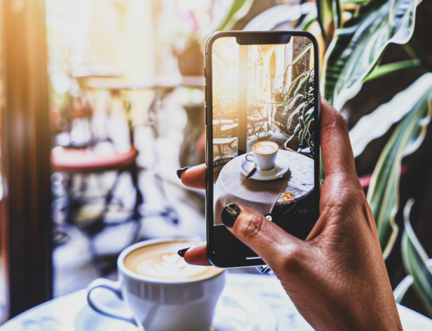 Milovník kávy zachytil fotografii latte art v živém prostředí kavárny se svěží zelení a teplým slunečním světlem.
