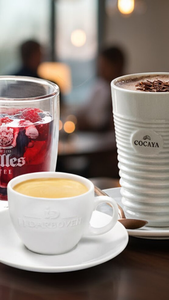 Bohatý výber kávy s espressom, horúcou čokoládou a ľadovým čajom na drevenom stole v živom prostredí kaviarne.