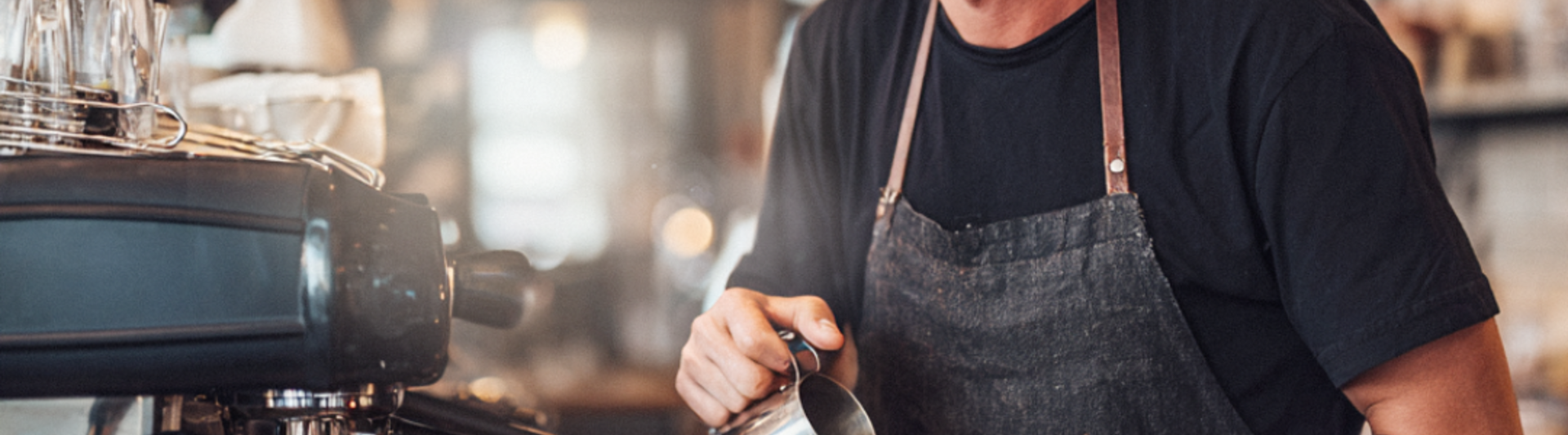 Uśmiechnięty barista nalewa latte art do filiżanki w modnej kawiarni, prezentując swoją wiedzę na temat kawy i pasję do jej parzenia.