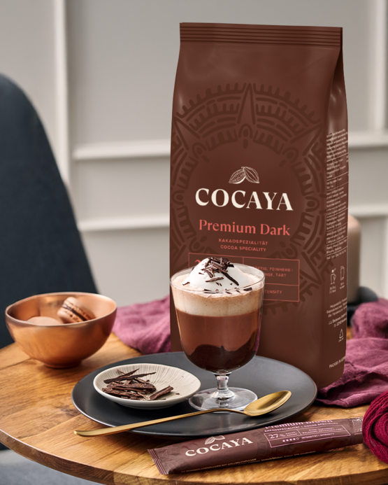 Kakaový prášek Cocaya Premium Dark s horkou čokoládou a makronkami na stylovém dřevěném stole.