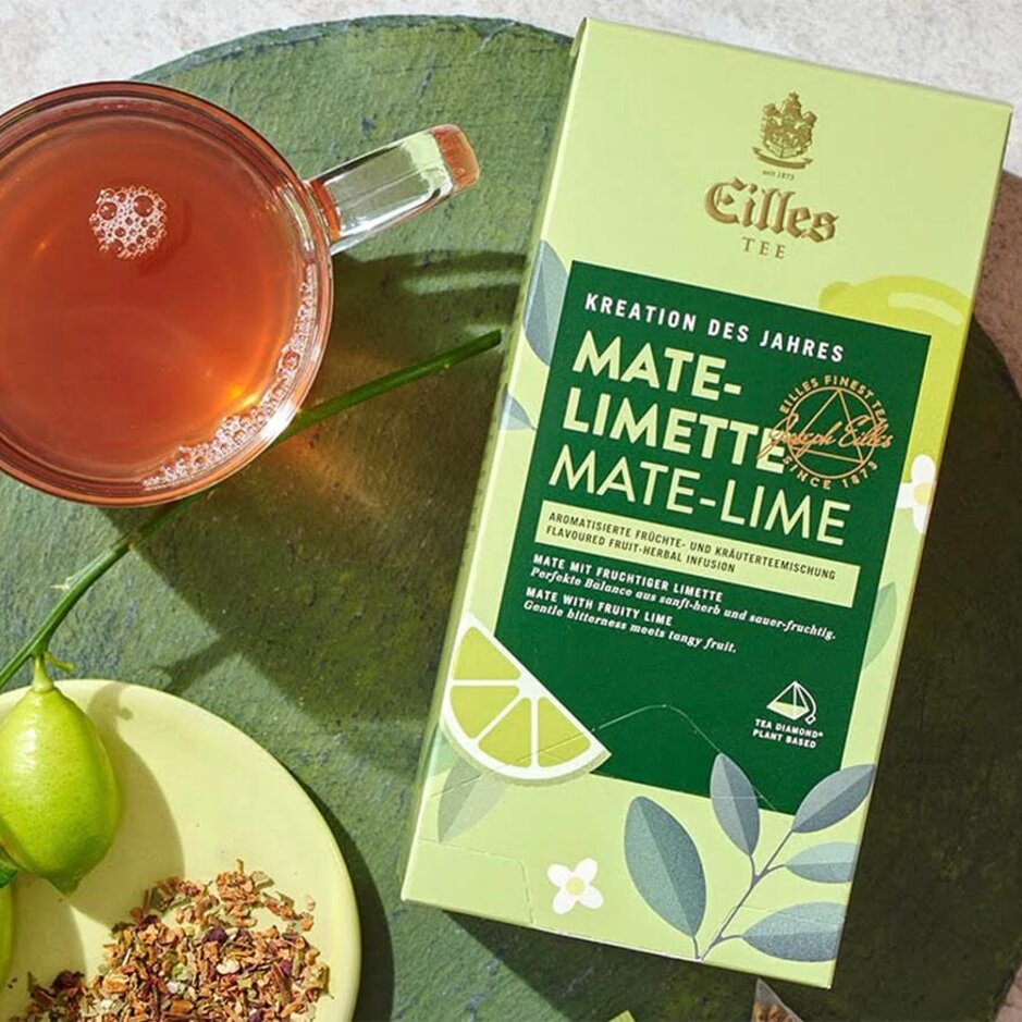 Čajová směs Mate-Lime od Eilles Tea s čerstvými limetkami a bylinným nálevem, podávaná na zářivě zeleném pozadí.