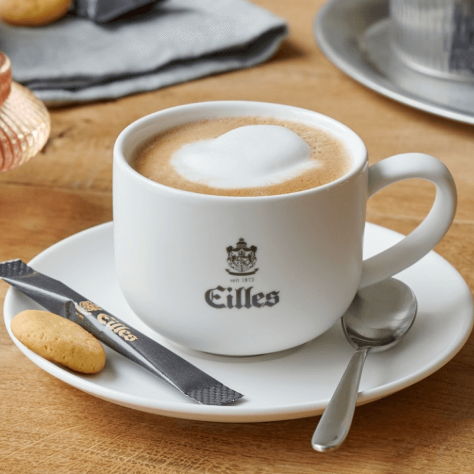 Krémová káva Eilles podávaná so sladkým pečivom a elegantným riadom je ideálna na príjemný zážitok v kaviarni.