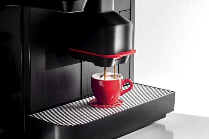 Kávovar Schaerer vaří espresso do stylového červeného šálku a ukazuje preciznost a kvalitu zpracování kávy.