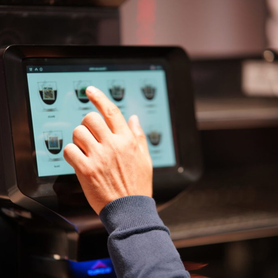Barista selecting drink options on a touchscreen coffee machine in a modern café setting.