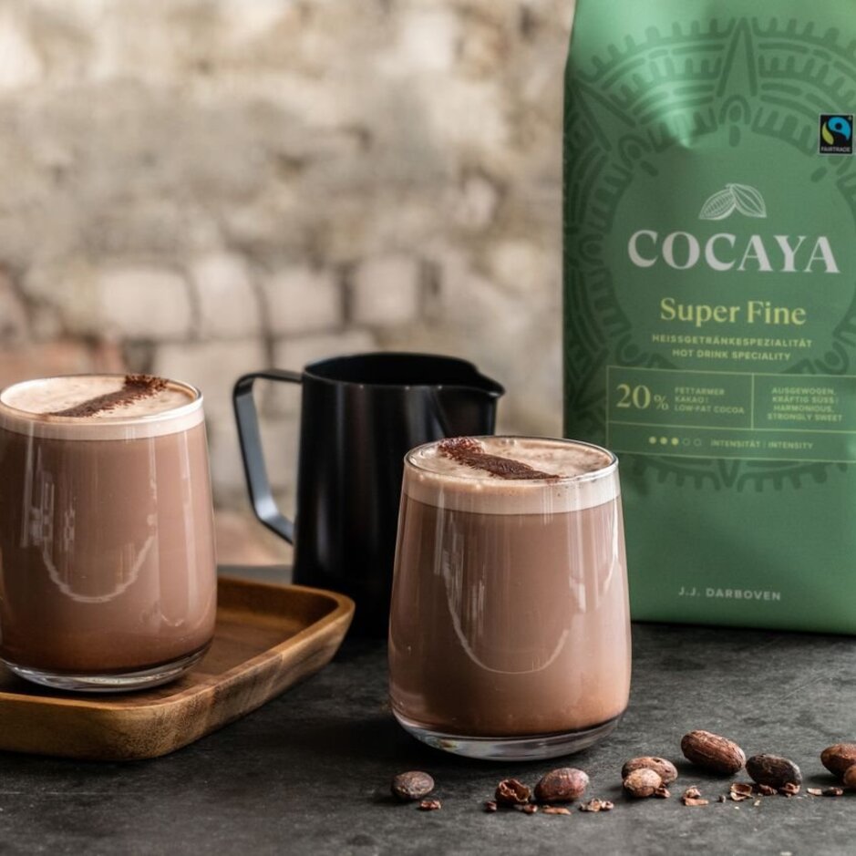 Rich hot cocoa served in elegant glasses, accompanied by cocoa beans and J.J. Darboven's Cocaya Super Fine blend.