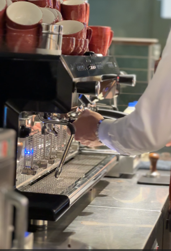 Barista preparing coffee with an espresso machine, surrounded by red cups in a stylish café setting.