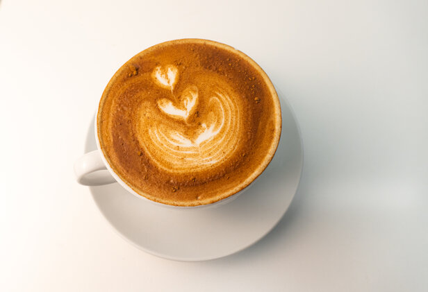 Creamy cappuccino with latte art in a white cup, served on a saucer against a light background.