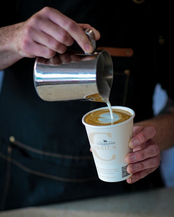 Barista pouring steamed milk into a cup, creating latte art in a stylish café setting. Ideal for coffee enthusiasts.