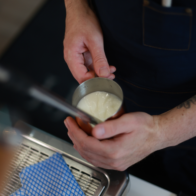 Barista preparing steamed milk in a metal jug, ready for crafting a perfect cappuccino or latte art.