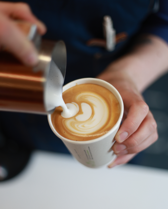 Barista pouring frothed milk into a cup of latte, creating a beautiful swirl pattern. Perfect for coffee lovers!