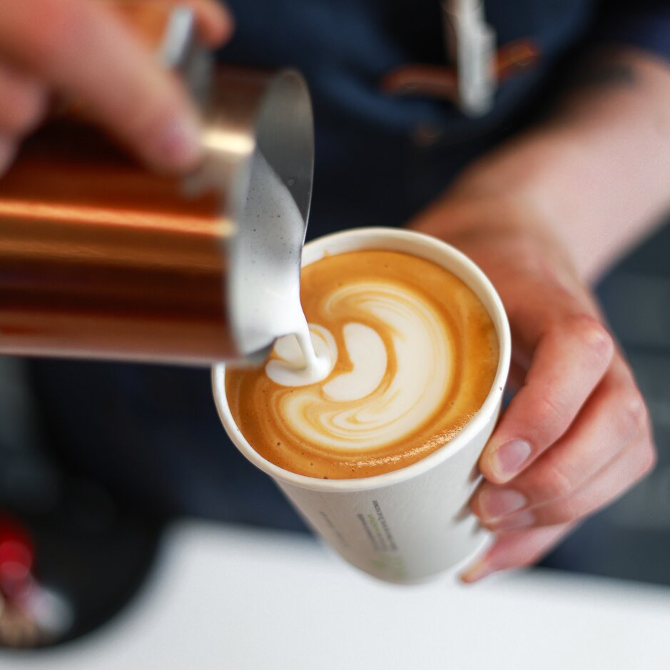 Barista pouring steamed milk into a cup, creating beautiful latte art with rich coffee and creamy froth.