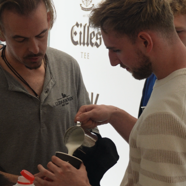 Baristas demonstrating milk frothing techniques at a coffee workshop, creating a perfect latte art experience.