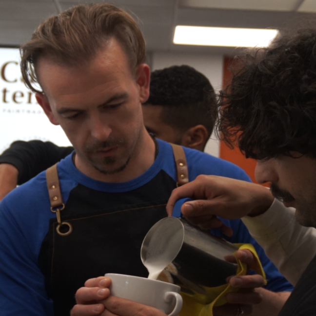Barista expertly pours steamed milk into a coffee cup during a barista training session in a café.