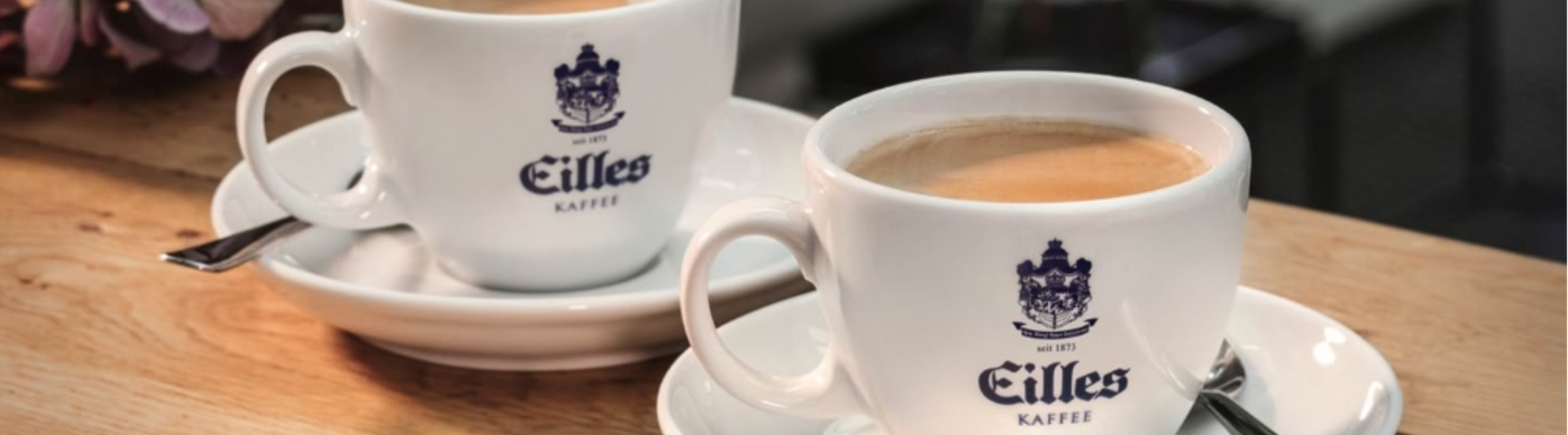 Two elegant cups of Eilles Kaffee coffee served on saucers, set against a warm wooden backdrop.