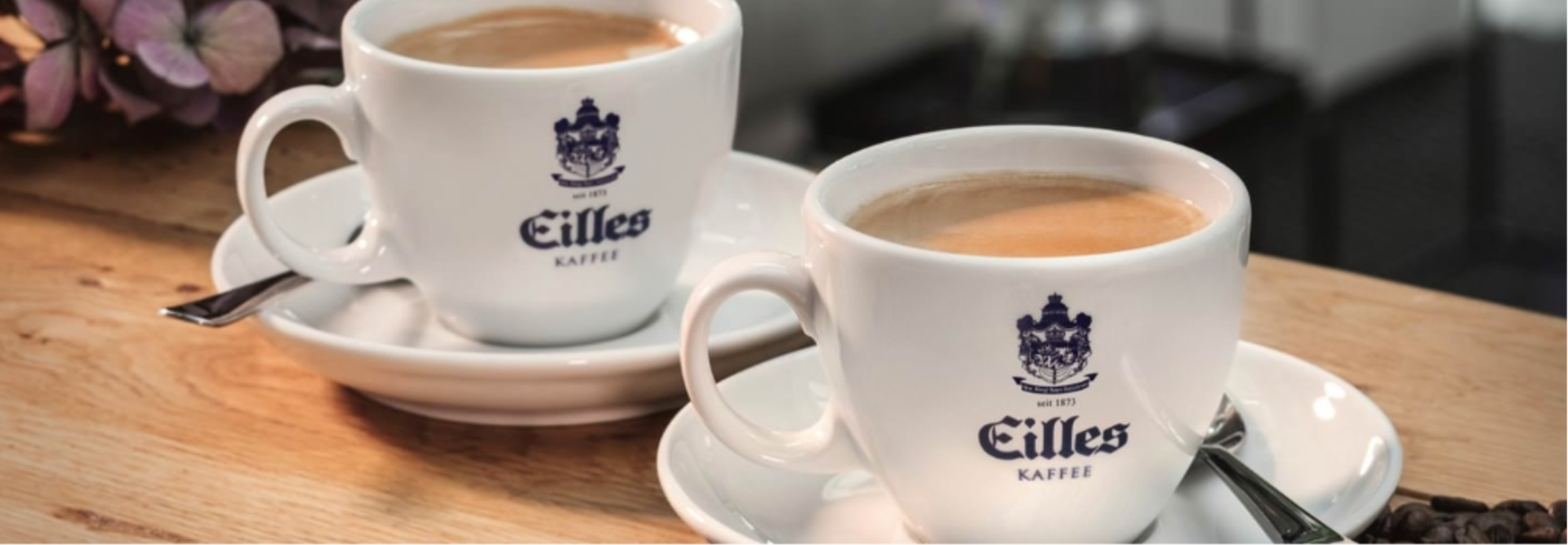 Two elegant cups of Eilles Kaffee coffee served on saucers, set against a warm wooden backdrop.