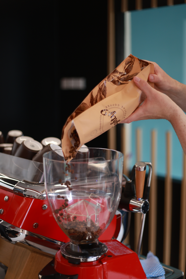 Barista pouring coffee beans from a bag into a grinder for fresh brewing in a modern café setting.