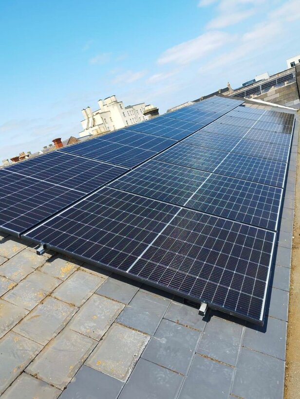 Solar panels installed on a slate roof, harnessing sustainable energy under a clear blue sky.