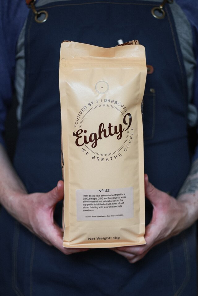A barista holds a 1kg bag of Eighty9 coffee, showcasing premium beans from Peru and Ethiopia, labelled No. 52.