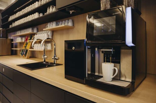 Modern coffee machine preparing a fresh brew in a stylish kitchen with neatly arranged cups on shelves.