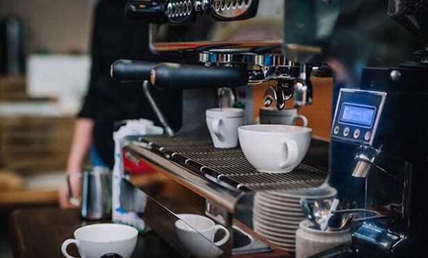 Coffee cups positioned under an espresso machine, ready for barista preparation in a stylish café setting.