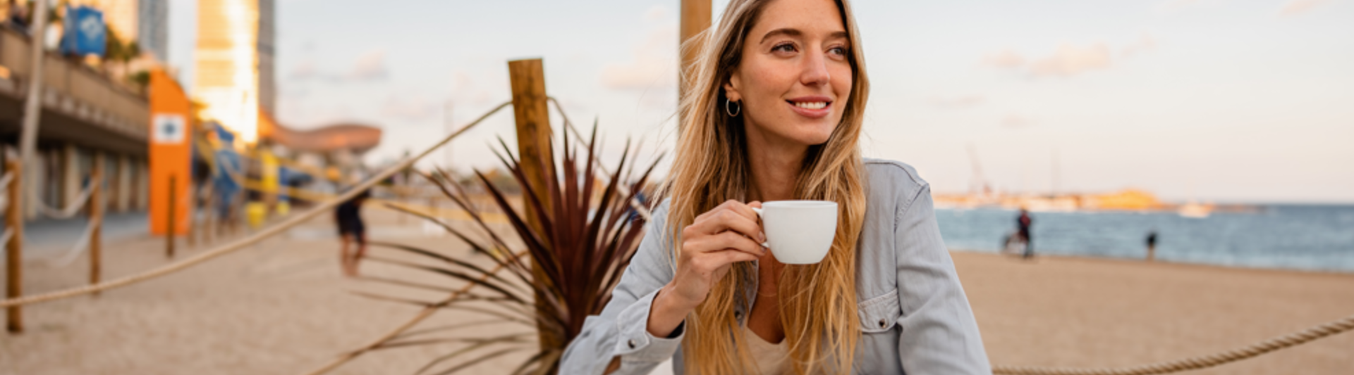 Femme détendue dégustant un café sur une plage de sable avec l'horizon de la ville en arrière-plan. Parfait pour les cafés côtiers.