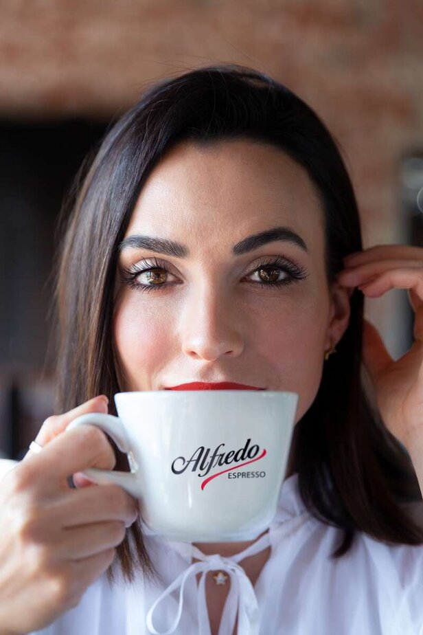 Femme dégustant une tasse d'Alfredo Espresso, mettant en valeur l'élégance et l'amour du café de qualité dans un décor de café lumineux.