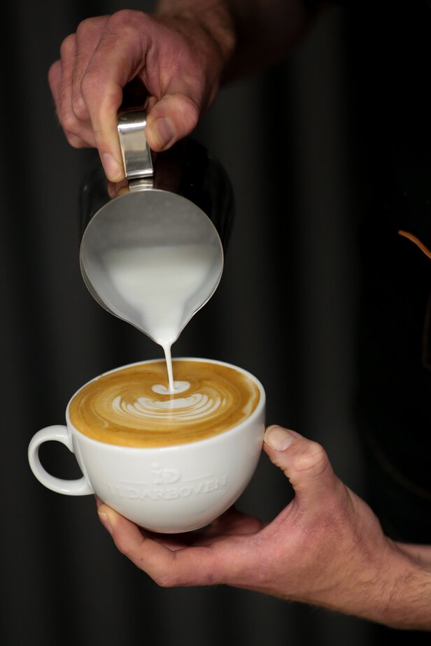 Barista versant du lait à la vapeur dans un café au lait, créant des motifs artistiques dans une tasse à café blanche.