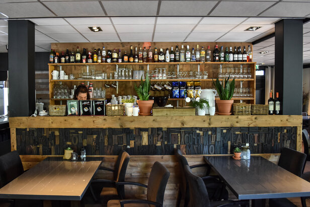 Stijlvol café-interieur met een houten bar, een selectie drankjes en planten in potten voor een gezellige sfeer.