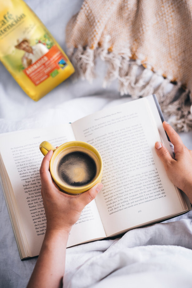Genieten van Cafe Intencion Aromatico-koffie terwijl je een boek leest, gewikkeld in een knus dekentje op een luie middag.