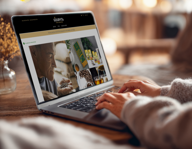 Gebruiker bladert door gastronomische voedingsproducten op een laptop en toont ambachtelijke koffie en verpakkingen. Gezellige binnenomgeving.