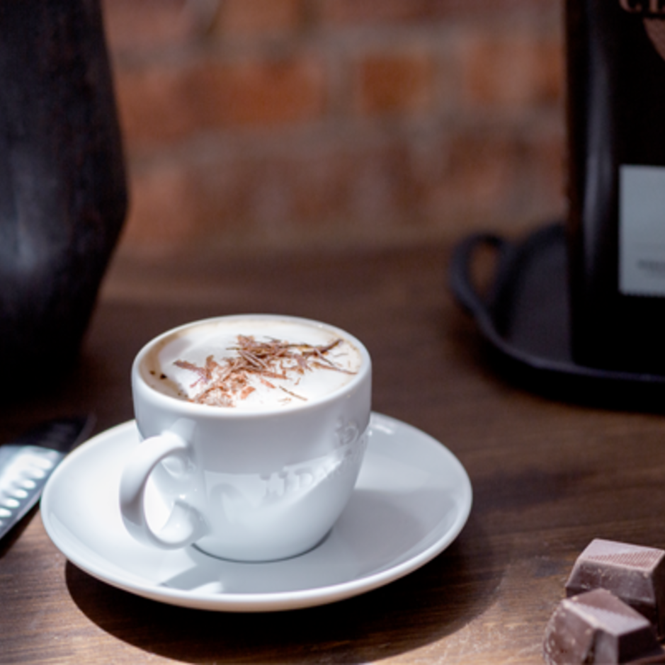 Rijke espresso overgoten met chocoladeschaafsel, geserveerd naast stukjes pure chocolade en een koffiezakje op een rustieke houten tafel.