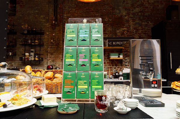 Een display met premium theedozen in een stijlvol café, met verschillende smaken naast gebak en glaswerk.