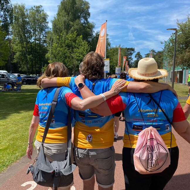 Deelnemers in kleurrijke t-shirts genieten samen van het HomeWalk 2024 evenement op een zonnige dag.