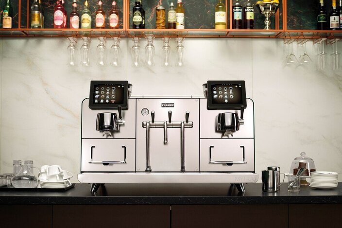 Strakke Franke Mytico Vario koffiemachine op een toonbank, ideaal voor hotelbars, met glaswerk en drankjes op de achtergrond.