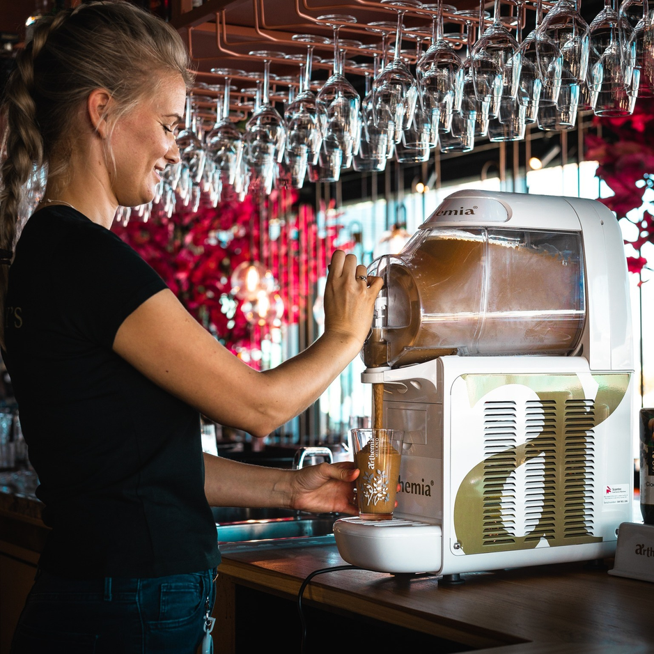 Barman serveert een drankje met de Sfeer Arthemia machine in een stijlvolle bar met levendig decor.