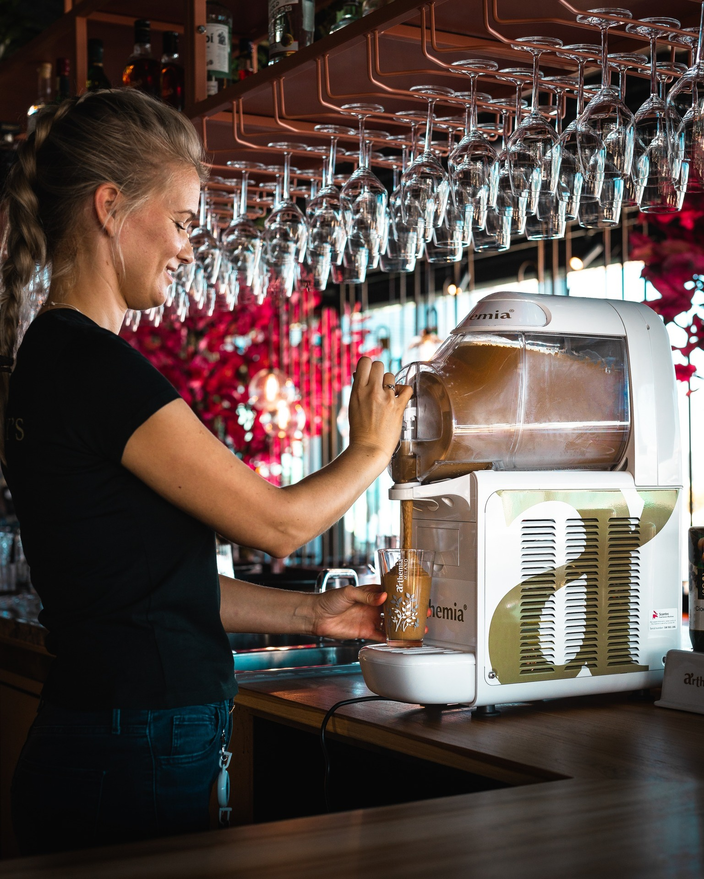 Barman serveert een drankje met de Sfeer Arthemia machine in een stijlvolle bar met levendig decor.