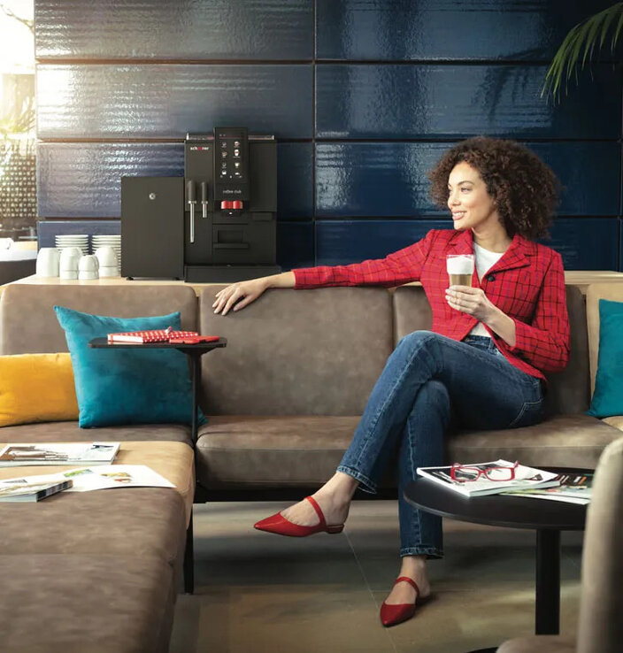 Een vrouw geniet van een kopje koffie in een stijlvol café, met op de achtergrond een Schaerer-koffiemachine.