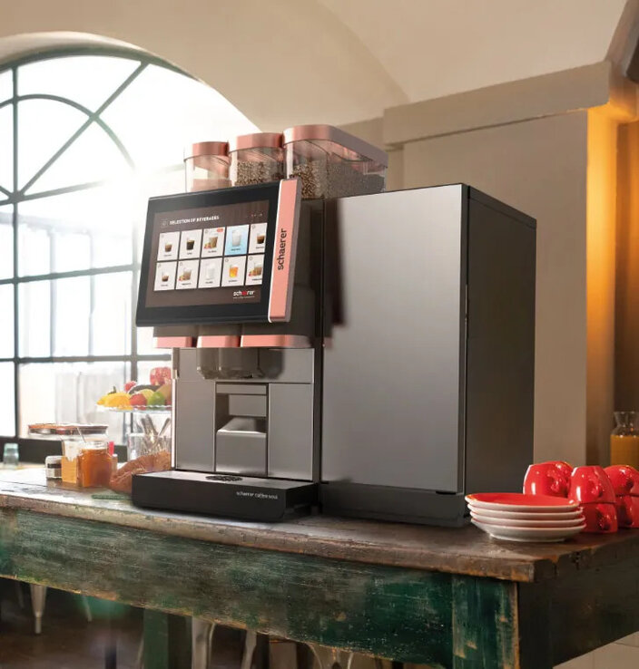 Een Schaerer-koffiemachine met touchscreen, geplaatst in een stijlvolle caféomgeving met een gevarieerd aanbod aan gerechten.