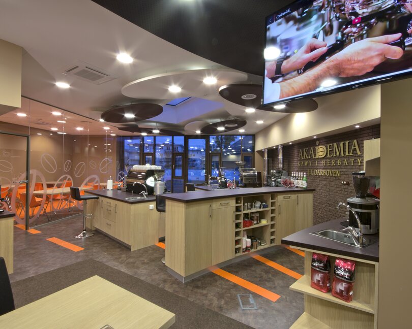 Nowoczesne wnętrze kawiarni z eleganckim wystrojem, żywymi pomarańczowymi akcentami i widokiem na sprzęt kawowy i siedzenia.