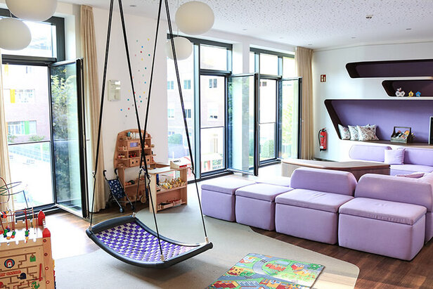 Jasny i zachęcający plac zabaw w Ronald McDonald House Hamburg, wyposażony w huśtawkę i miękkie siedzenia dla dzieci.