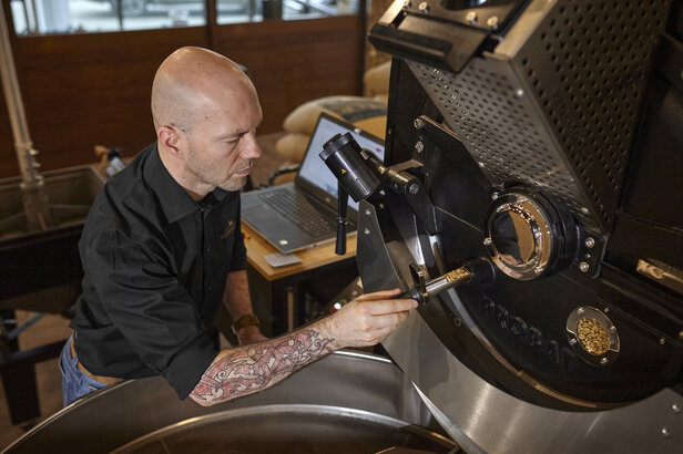 Barista monitorujący proces palenia kawy, prezentujący doświadczenie w rzemieślniczym przygotowywaniu kawy i technikach palenia.