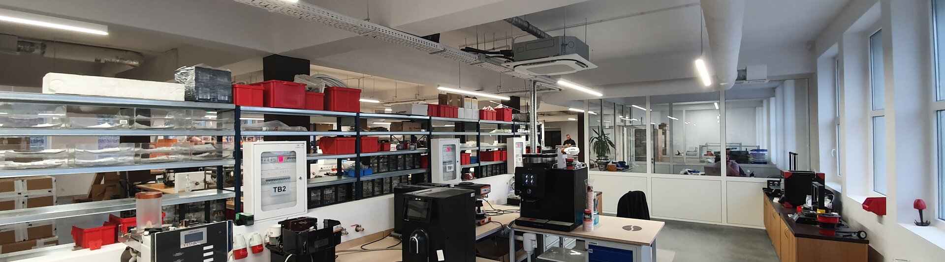Nowoczesna przestrzeń robocza w laboratorium, wyposażona w komputery, sprzęt i uporządkowane schowki, o jasnym, funkcjonalnym wystroju.