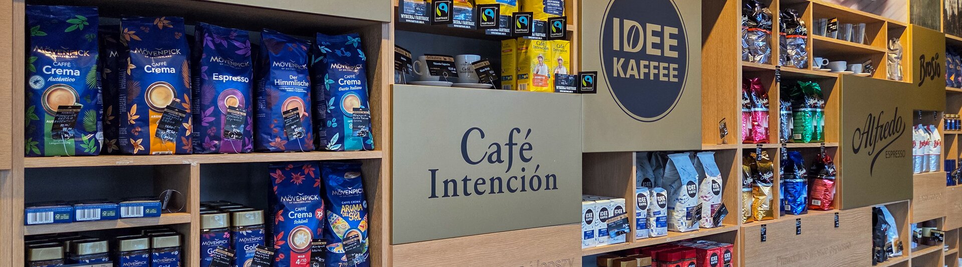 Ekspozycja produktów Mövenpick i Idee Kaffee, prezentująca gatunki kawy premium na drewnianych półkach.