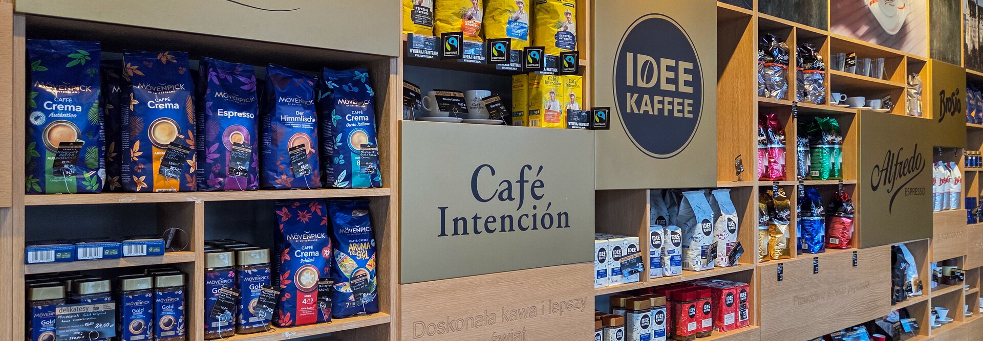 Ekspozycja produktów Mövenpick i Idee Kaffee, prezentująca gatunki kawy premium na drewnianych półkach.