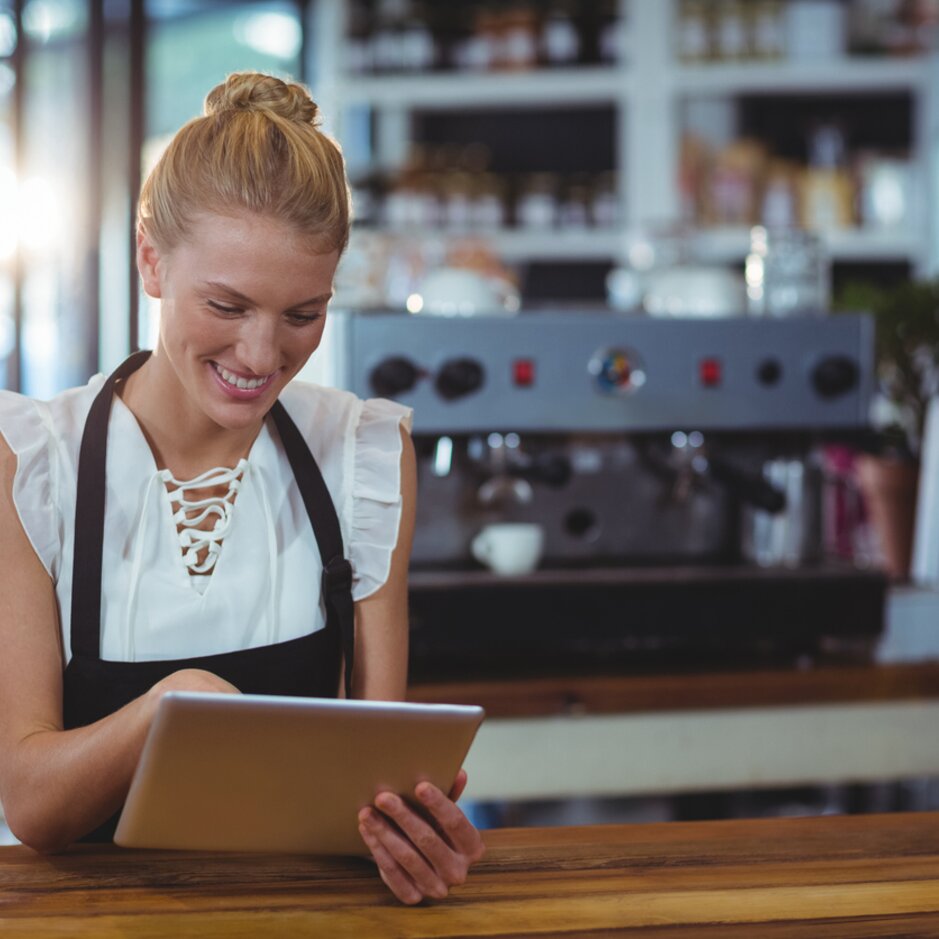 Barista korzystający z tabletu w kawiarni, uśmiechający się i angażujący klientów w otoczeniu wypieków.
