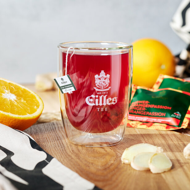 Szklanka herbaty Eilles z pomarańczą i imbirem na drewnianym stole, idealna na jesienne ciepło i smakowy komfort.