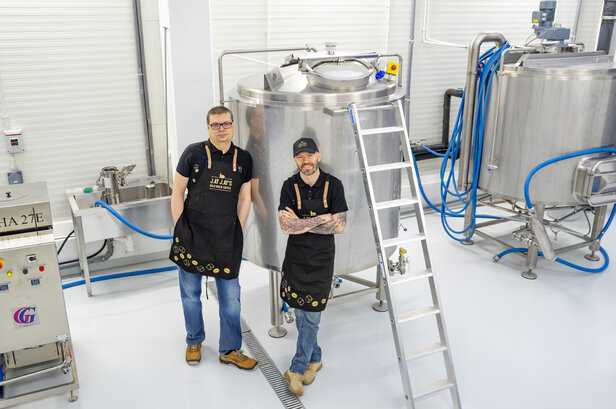 Dwóch baristów w fartuchach stoi w nowoczesnym punkcie parzenia kawy ze sprzętem ze stali nierdzewnej.