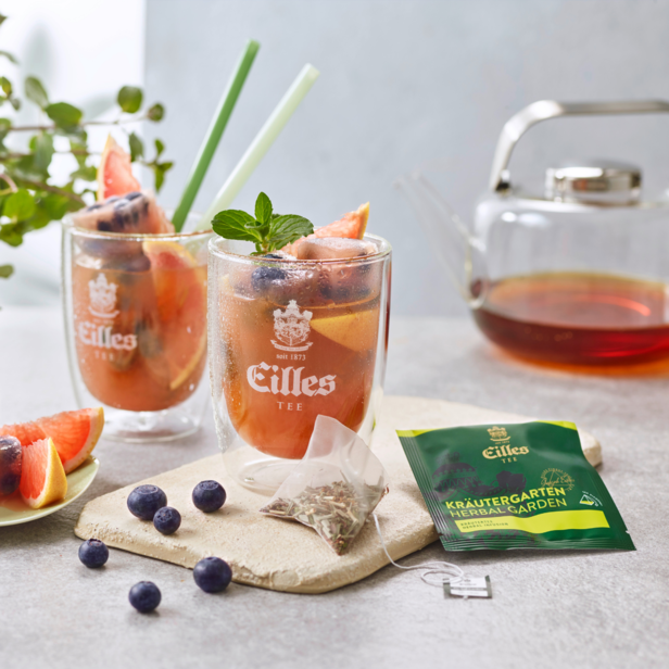 Orzeźwiająca herbata Eilles Kräutergarten podawana z owocami, prezentująca żywą mieszankę ziół i eleganckie szkło.