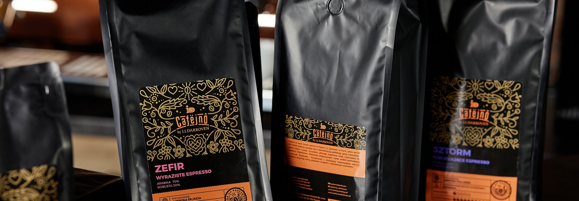 Worki kawy Caféjno, w tym Zefir i Sztorm, wystawione z palonymi ziarnami na ladzie. Idealne dla miłośników kawy.